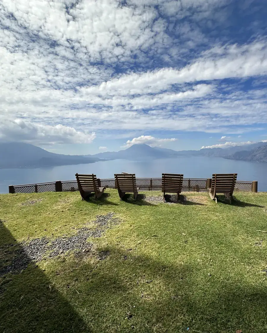 Sillas de madera en el pasto del mirador, mirando hacia el lago y los volcanes